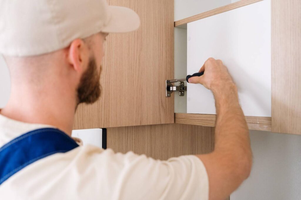 A man is seen installing a cabinet in a room carefully securing it to the wall for stability