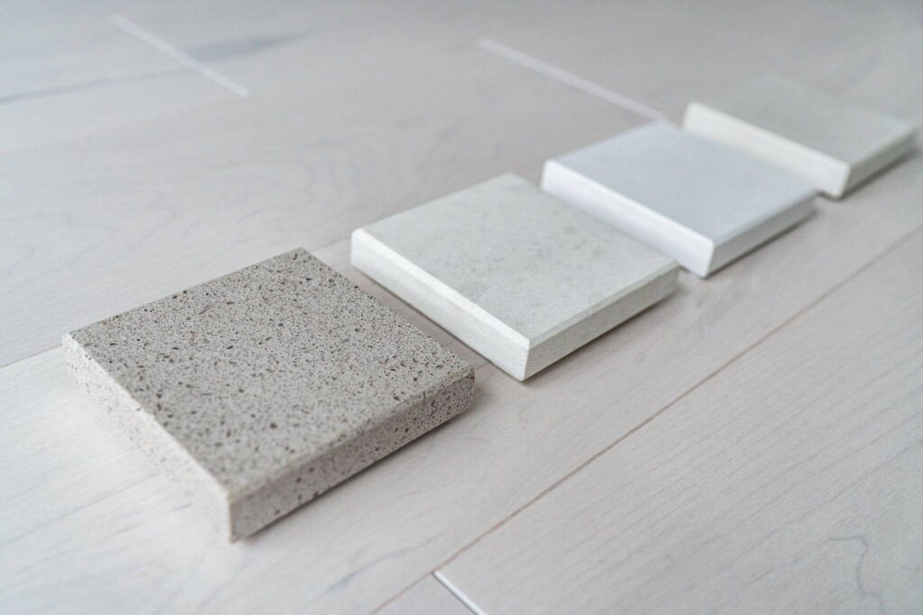 Four square stone samples in shades from light gray to beige are lined up diagonally on a light wood surface