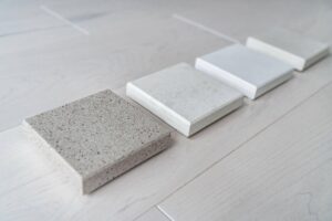 Four square stone samples in shades from light gray to beige are lined up diagonally on a light wood surface