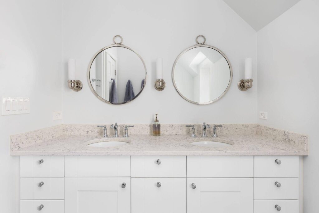 Minimalist bathroom with two round mirrors above a white dual-sink vanity