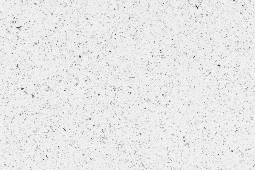 A close-up texture shot of a white quartz countertop with grey and black speckles.