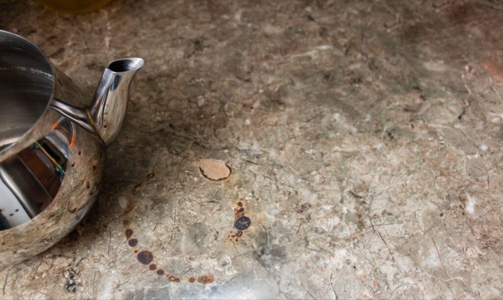 A silver tea pot elegantly placed on a kitchen counter reflecting light from nearby windows