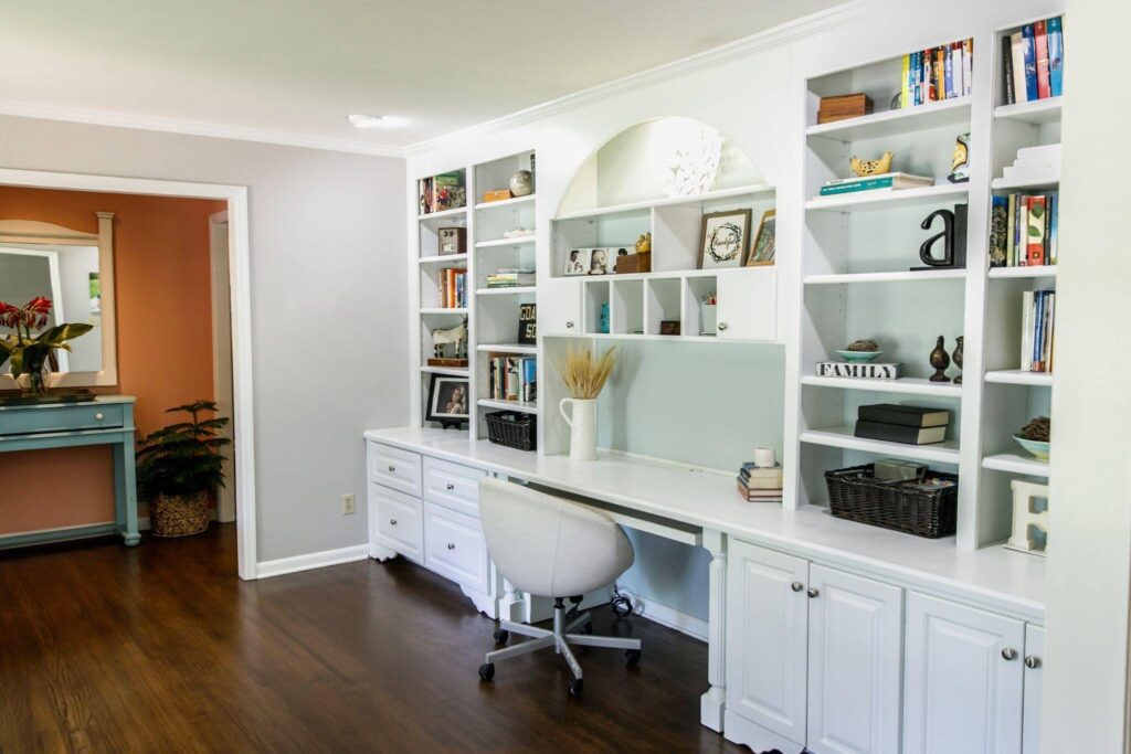 A bright home office showcasing a sleek desk and two bookshelves lined with a variety of books and decorative items