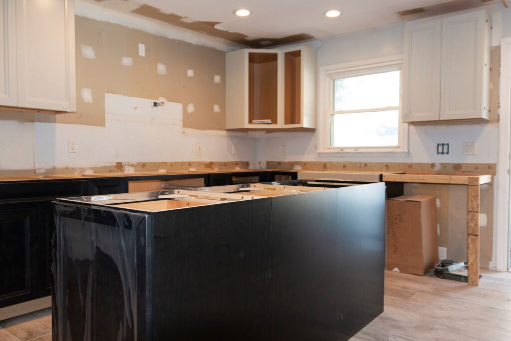 A kitchen undergoing renovation with unfinished walls, cabinets, and a large central island frame.