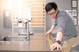 A man is carefully measuring a countertop with a ruler assessing its size for a project