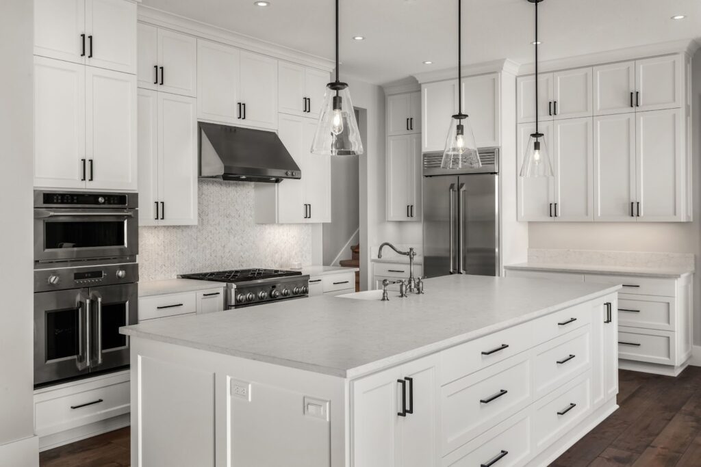 Modern kitchen with white cabinets, stainless steel appliances, a large island, and pendant lighting.