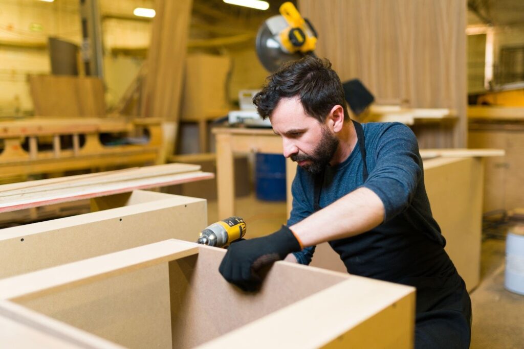 A man assembling furniture in a factory focused on his work with tools and materials around him