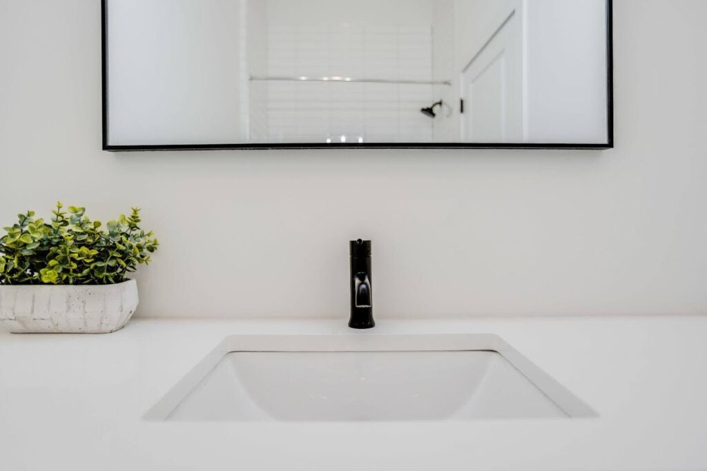 A clean bathroom sink featuring a mirror and a decorative plant placed beside it