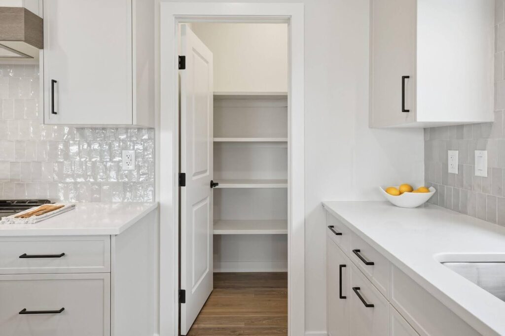 A modern kitchen features white cabinets black handles a tiled backsplash and a bowl of lemons
