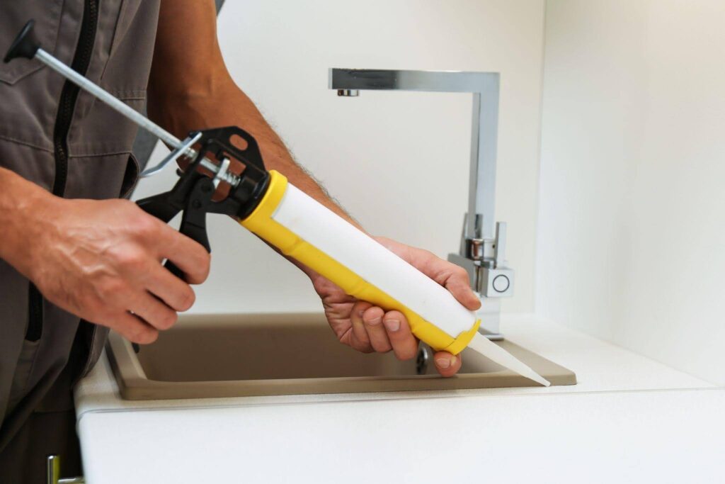 A man repairs a sink using a yellow and white tool focused on fixing the plumbing issue