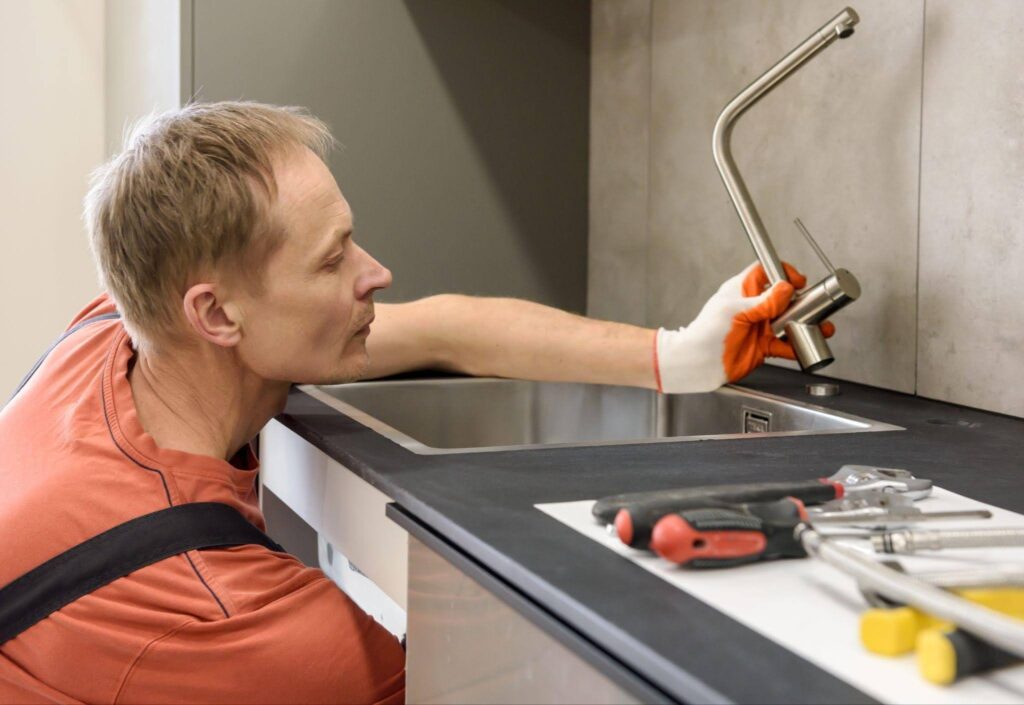 A man works on a sink applying tools to repair the plumbing effectively