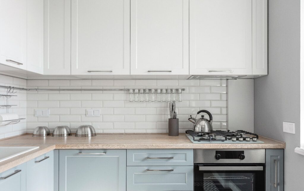 Bright kitchen counter with light blue lower cabinets, white upper cabinets, and a white subway tile backsplash.