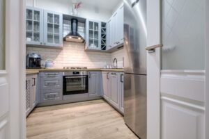Compact modern kitchen with grey cabinetry, stainless steel refrigerator, and black range hood.