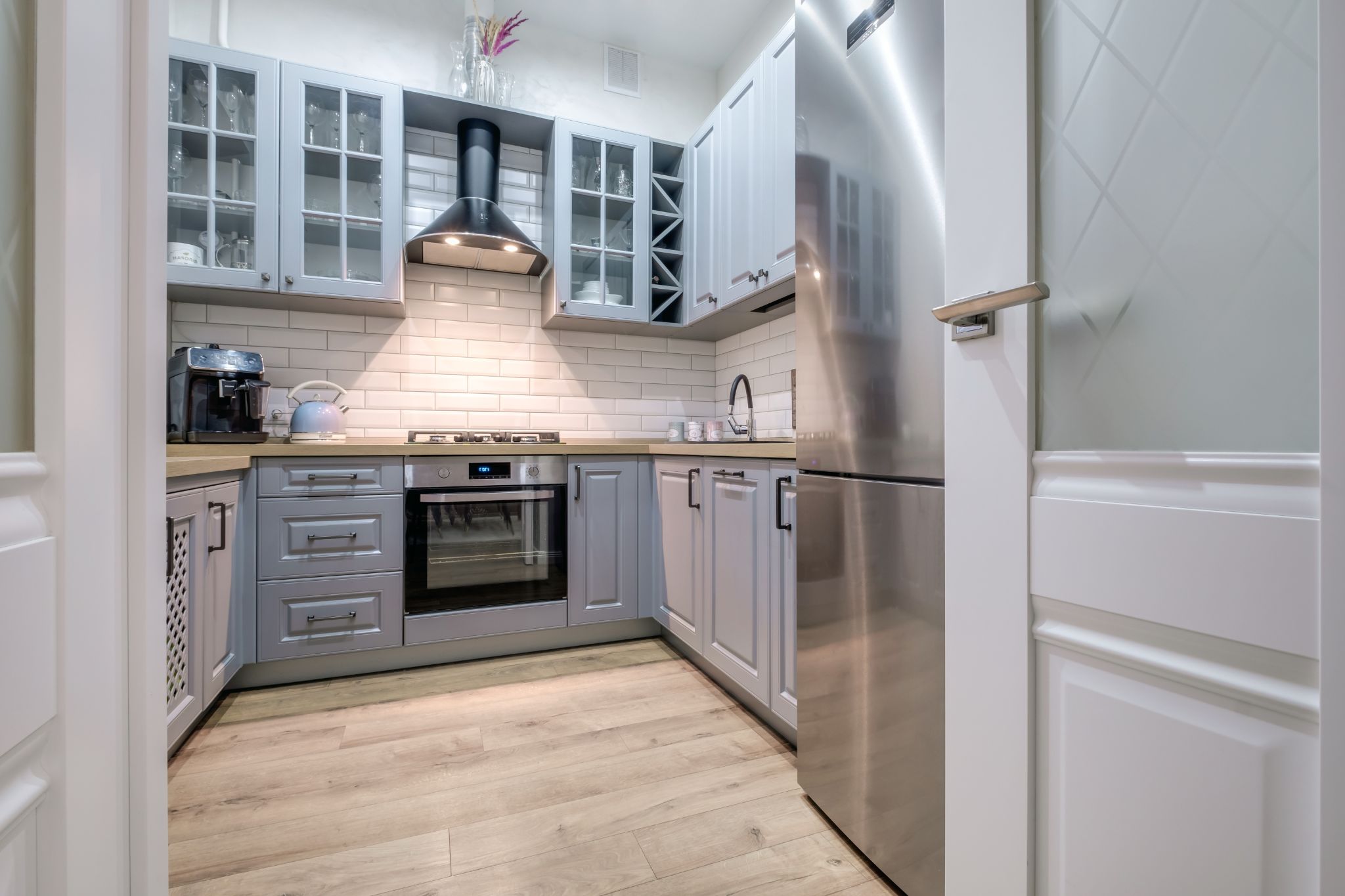 Compact modern kitchen with grey cabinetry, stainless steel refrigerator, and black range hood.