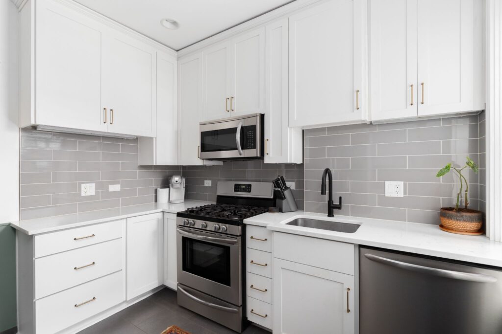 Modern kitchen featuring white cabinets, grey subway tile backsplash, and stainless steel appliances.