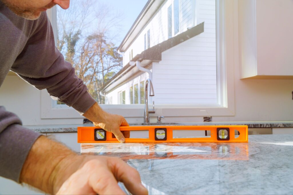 Contractor using an orange spirit level to check the alignment of a newly installed granite countertop.