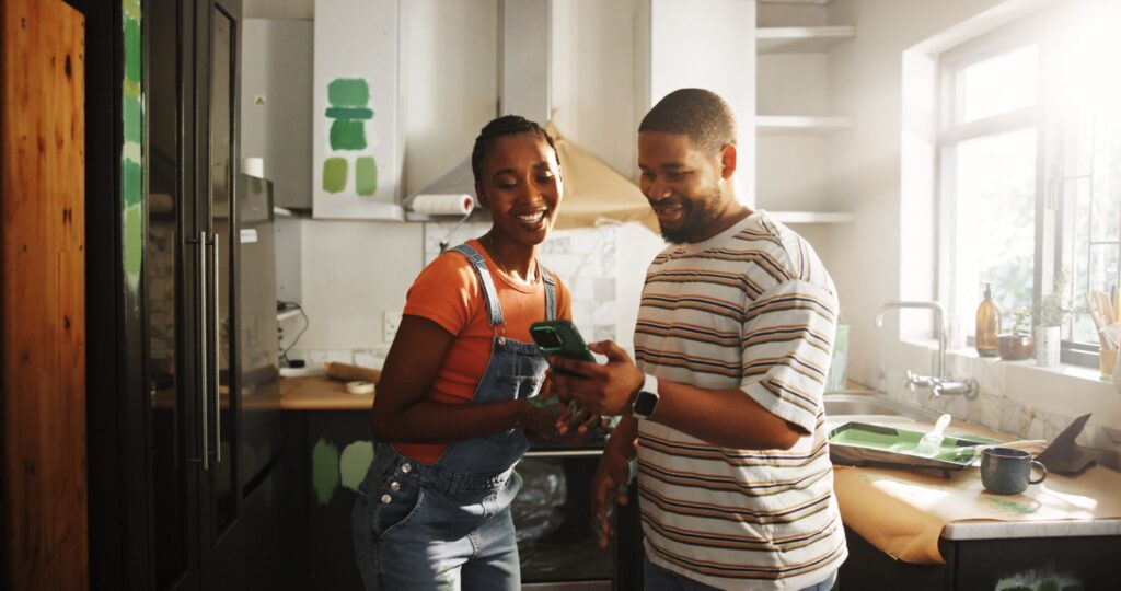 Couple looking at a smartphone while painting their kitchen