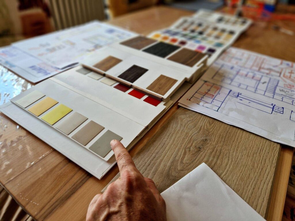 A hand points to a paint sample on a table highlighting a color selection for interior design